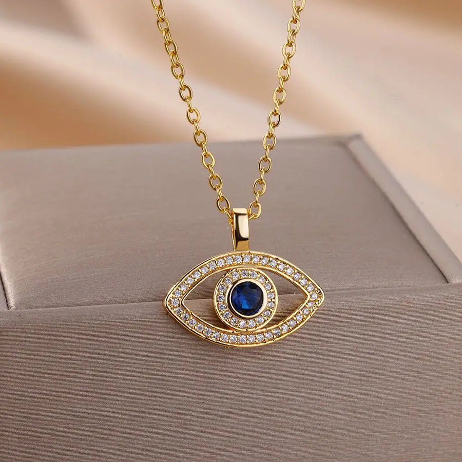Gold necklace with an eye-shaped pendant featuring a blue gemstone on a beige surface.