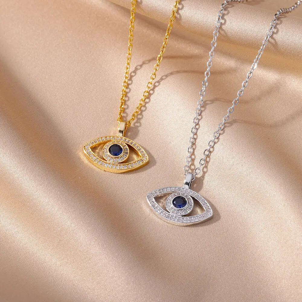 Two eye-shaped pendants on gold and silver chains on a beige fabric background